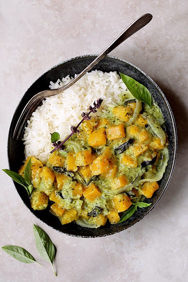 Photo of Butternut Squash in Fresh Green Curry with rice in black bowl garnished with Thai basil.
