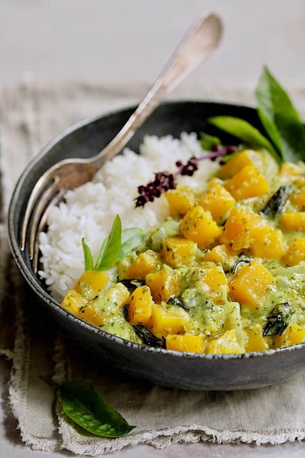 Photo of Butternut Squash in Fresh Green Curry in black bowl with rice garnished with Thai basil.