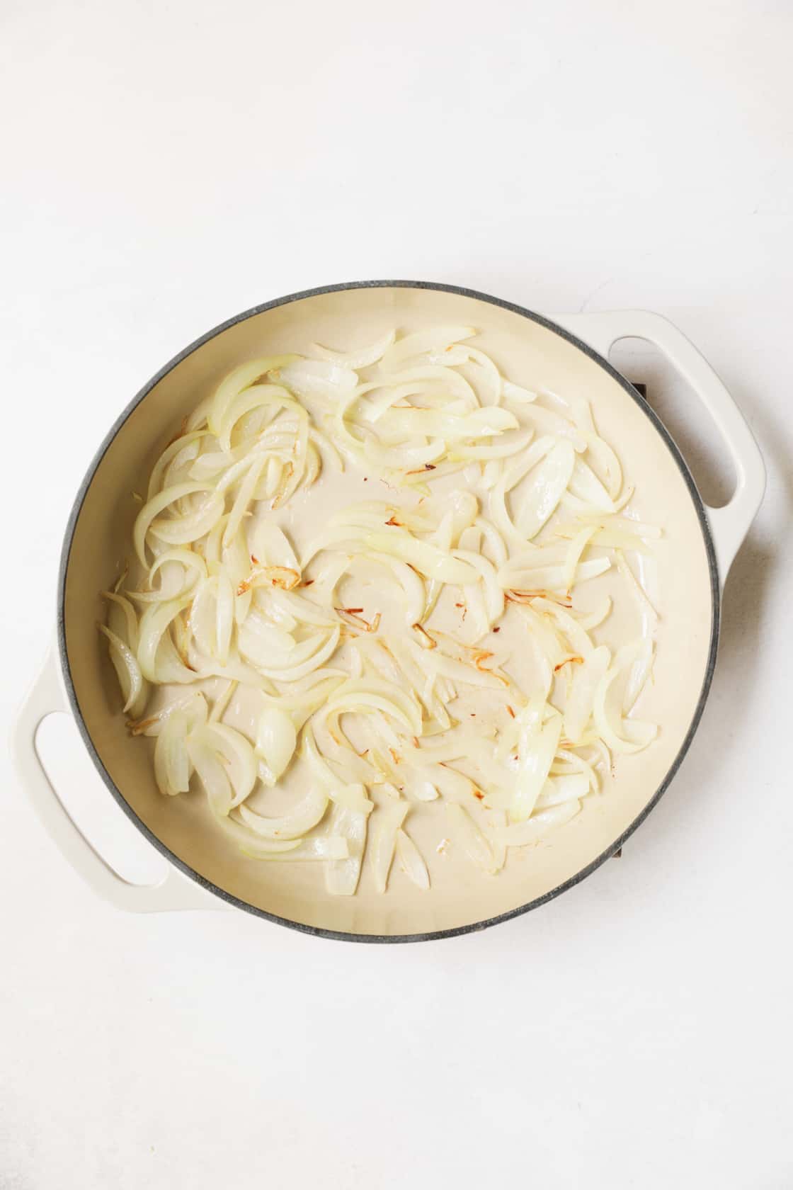 Photo of onions being cooked in white cast iron skillet.