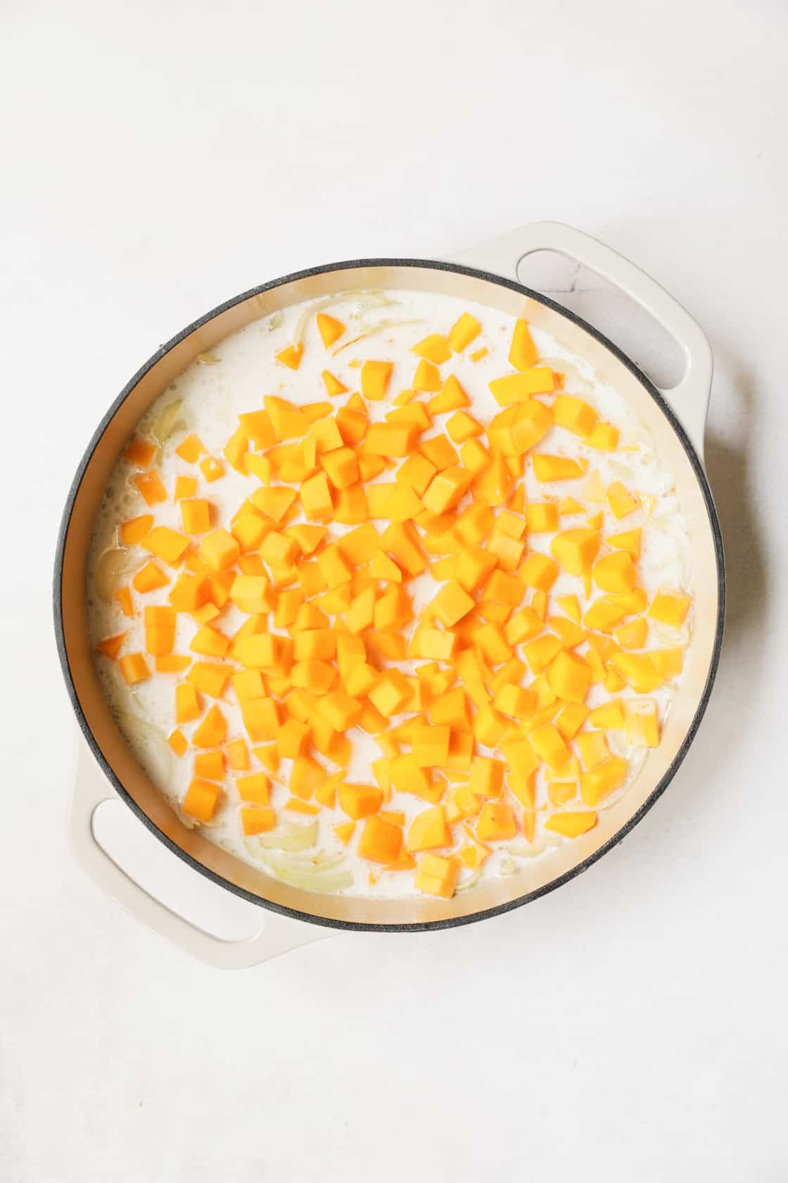 Photo of butternut squash being cooked in coconut milk in white cast iron pan.
