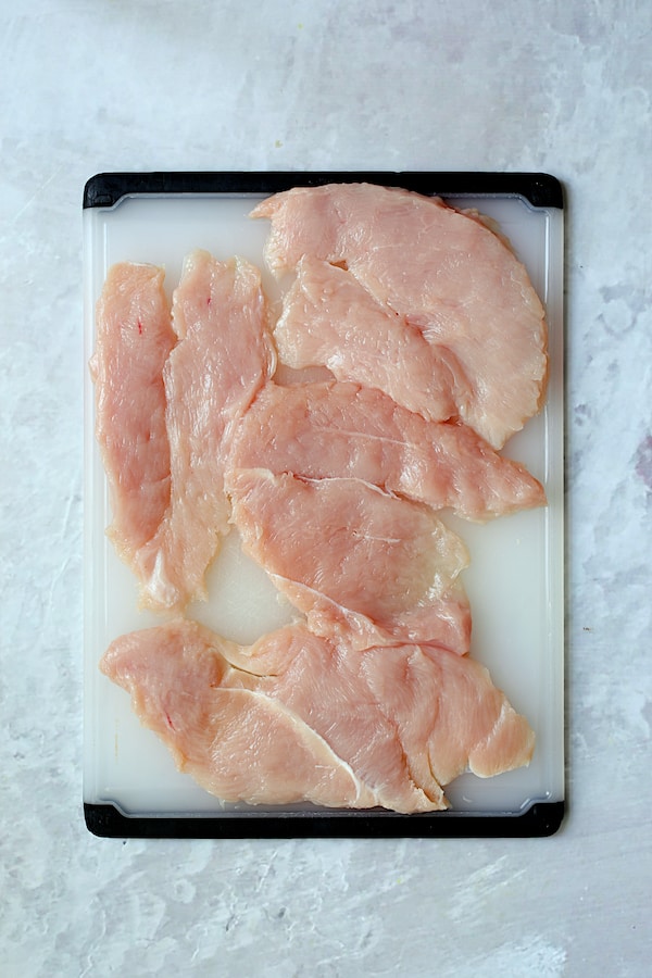 Overhead shot of turkey cutlets on white plastic cutting board
