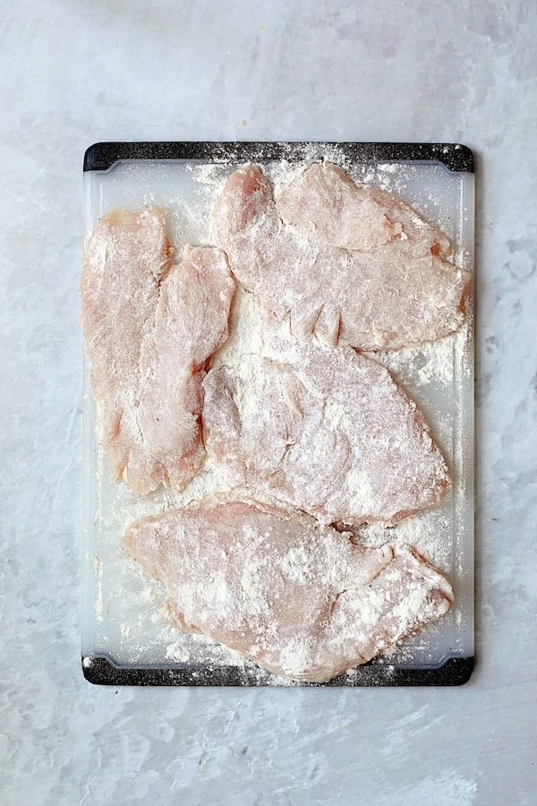 Overhead shot of turkey cutlets on white cutting board that have been dredged in flour