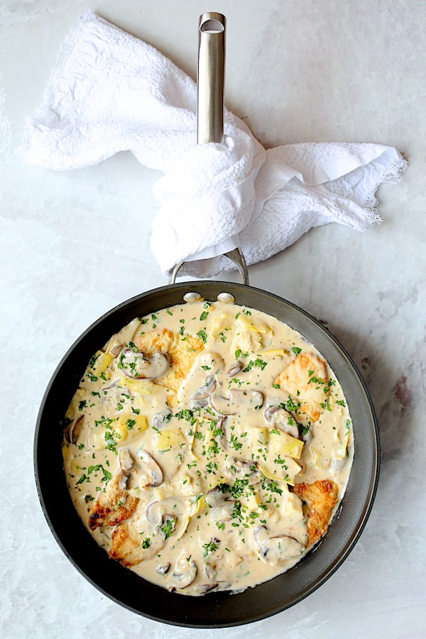 Turkey Scallopini in Sherry Cream Sauce with Mushrooms and Artichoke Hearts - Overhead shot of finished dish in skillet with white towel wrapped around handle