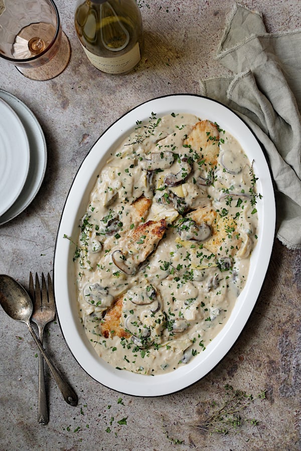 Turkey Scallopini in Sherry Cream Sauce with Mushrooms and Artichokes - Overhead shot of finished dish with platter at an angle with wine bottle, glass, serving utensils and napkin
