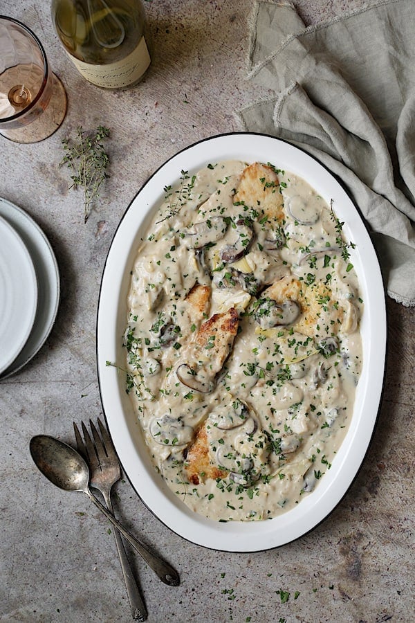 Turkey Scallopini in Sherry Cream Sauce with Mushrooms and Artichoke Hearts - Overhead shot of dish on white platter and gray stone background
