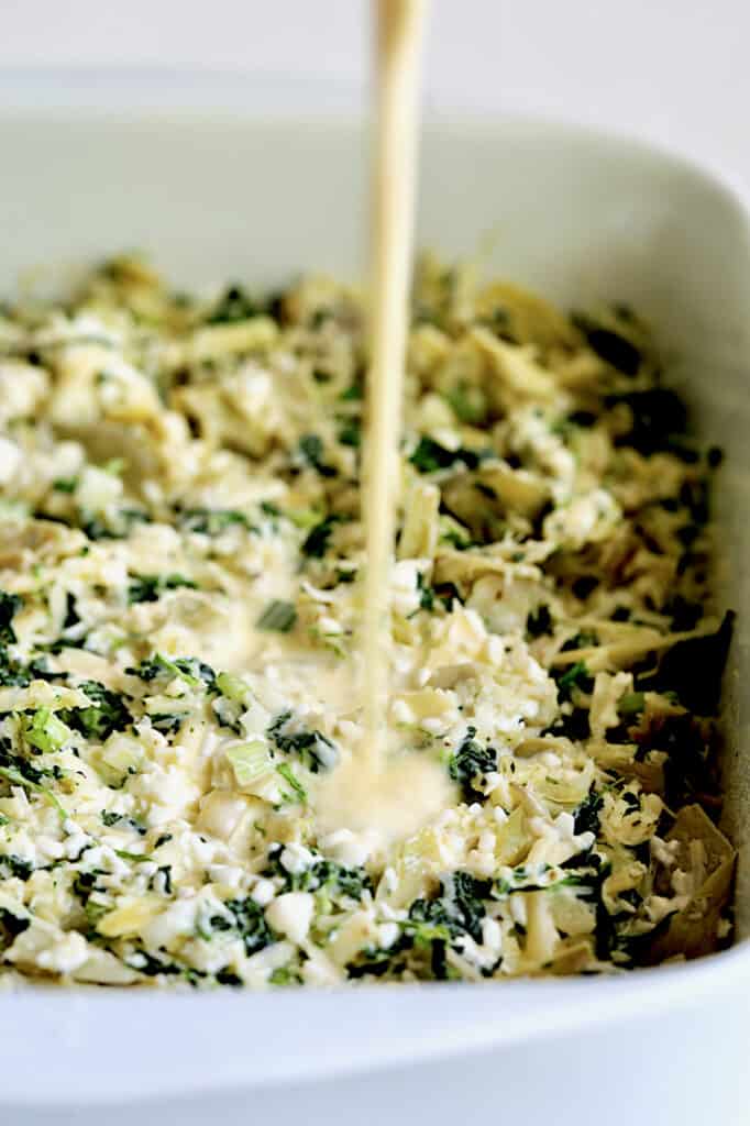 Photo of custard combination being poured over spinach artichoke combination.