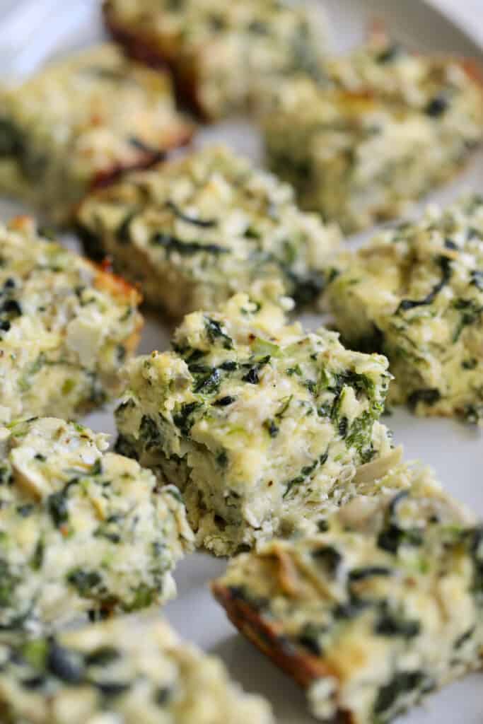 Close-up photo of Spinach Artichoke Squares on white platter.
