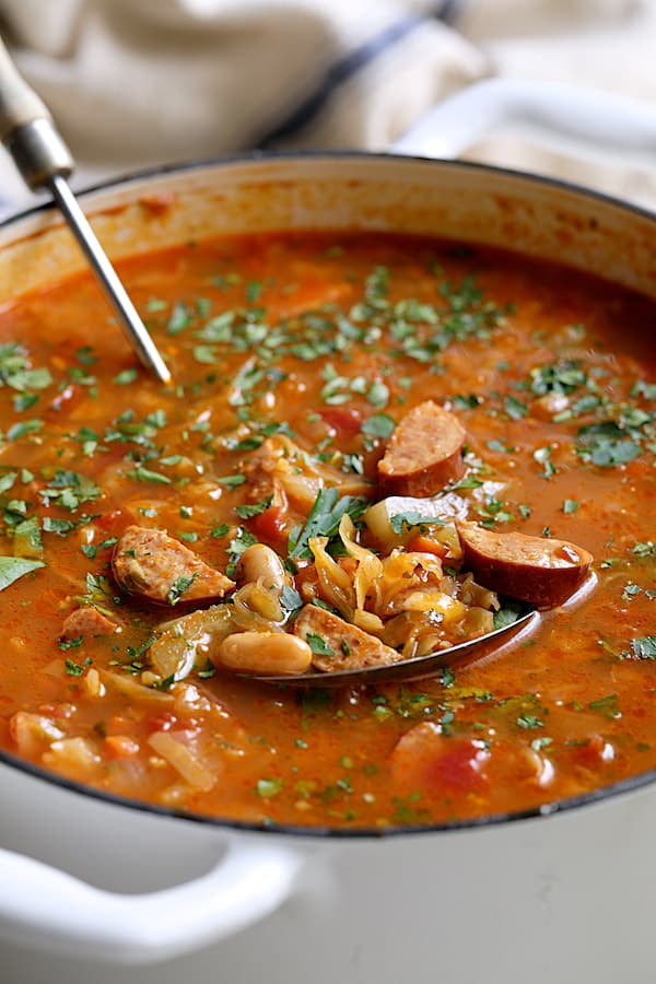 Close-up photo of Farmhouse Cabbage Soup with Cannellini Beans and Kielbasa in white Dutch oven.