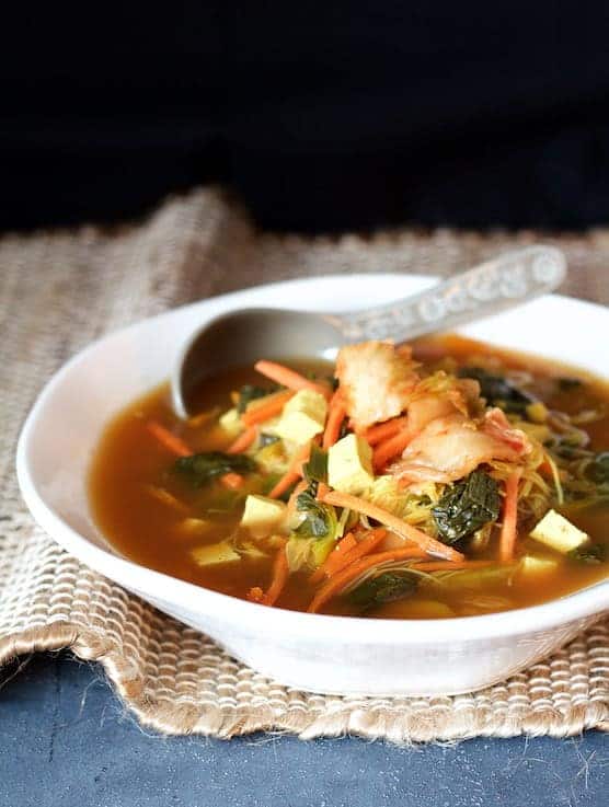 Asian Vegetable Soup with Tofu, Kimchi and Rice Noodles in white bowl on woven surface.