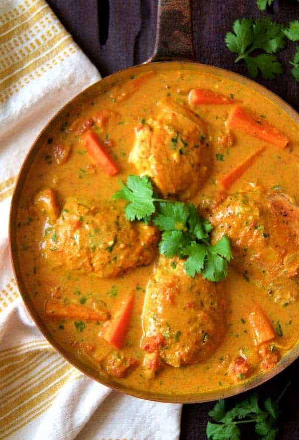 Curry Braised Chicken Thighs hero shot in pan garnished with cilantro on dark wood surface with yellow striped towel.