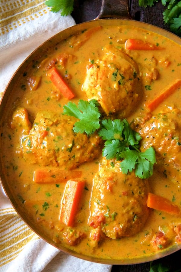 Photo of Curry Braised Chicken Thighs in skillet with carrots garnished with cilantro sprigs.