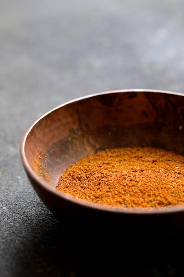 Photo of Madras curry powder blend in copper bowl on gray background.