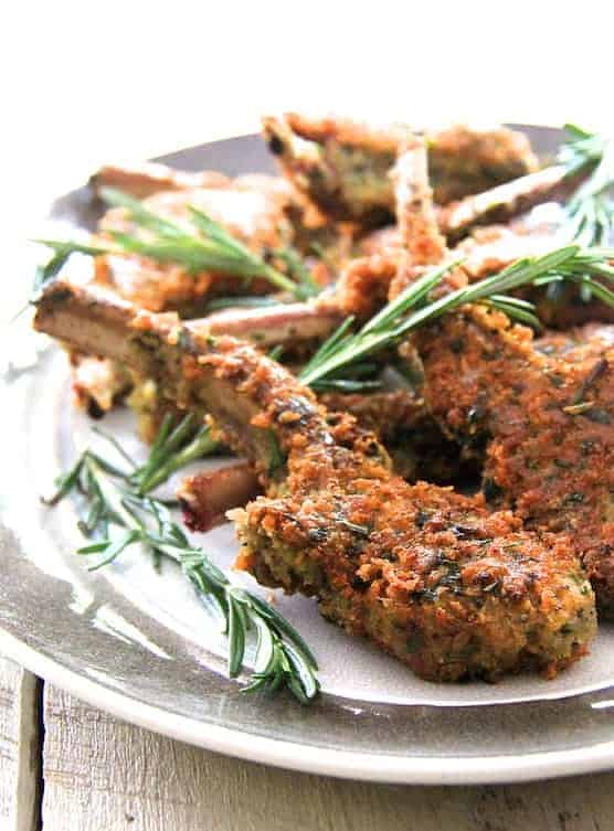 Parmesan and Herb Crusted Lamb Chops on gray-rimmed platter garnished with rosemary sprigs.
