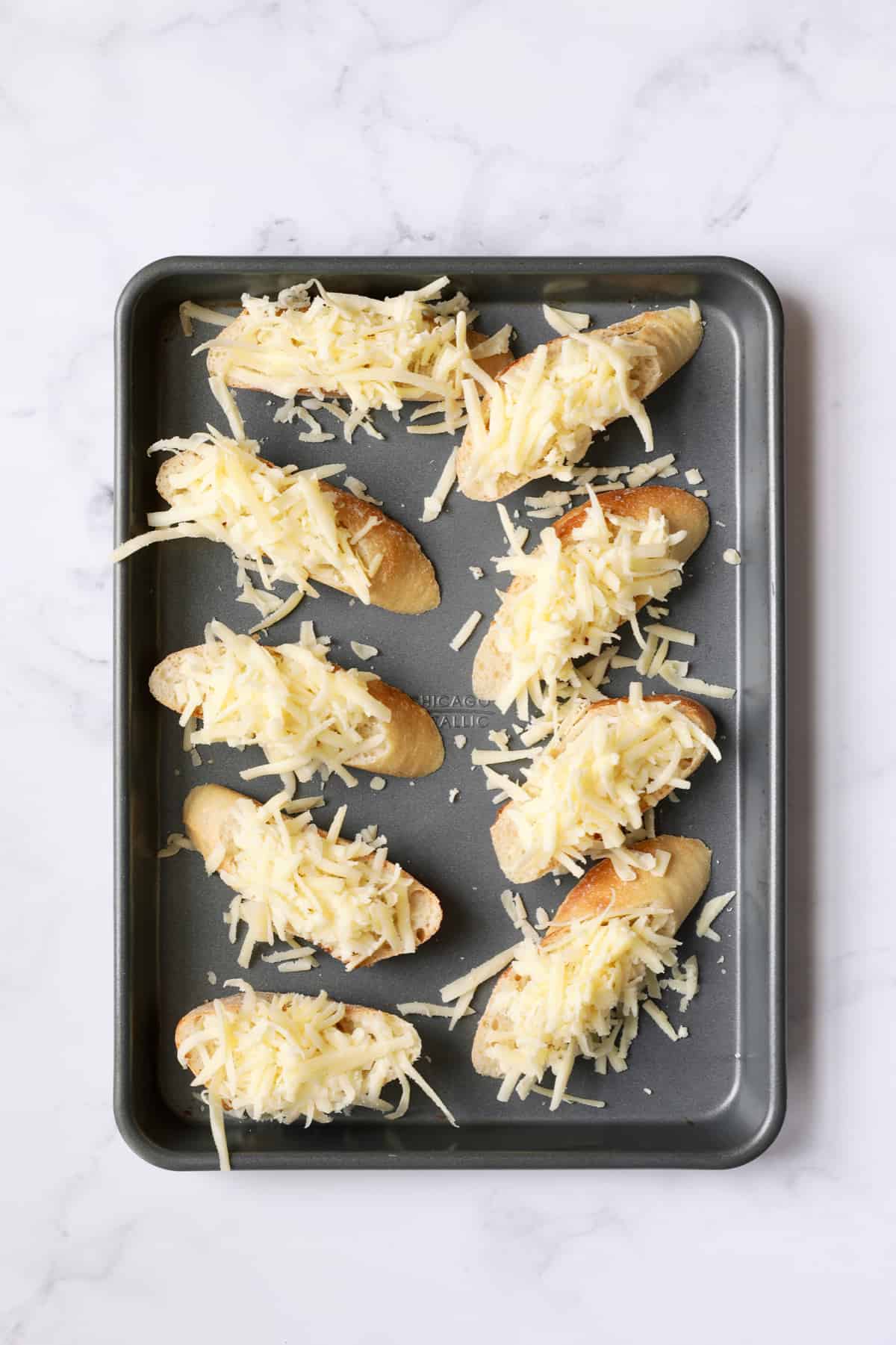 Overhead shot of 9 slices of French bread with cheese on top before placing in the oven