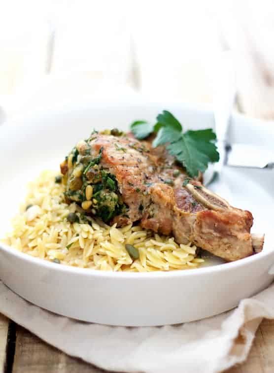 Photo of Sicilian-Stuffed Pork Chops with White Wine Caper Sauce and orzo garnished with parsley.