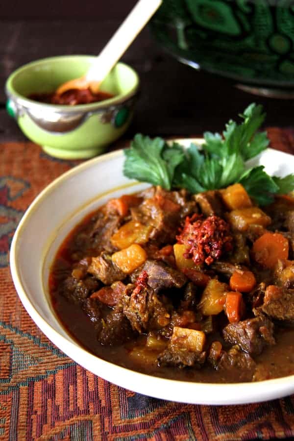 Photo of Moroccan Beef Stew with Harissa in white bowl garnished with celery leaves.