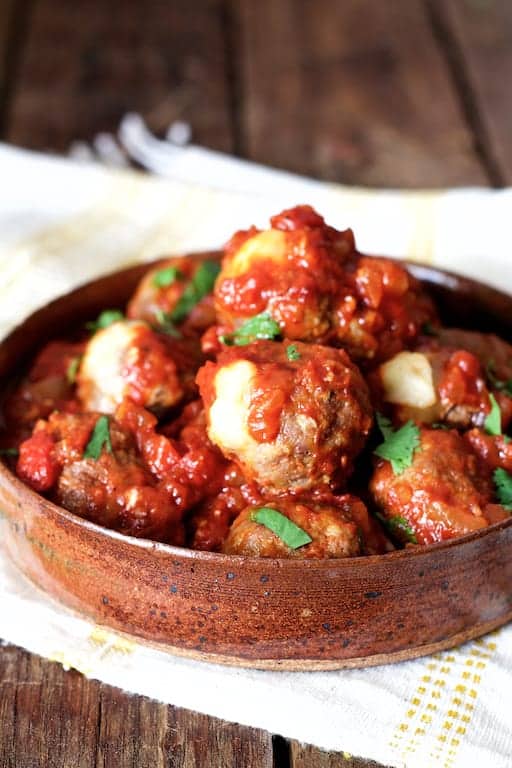 Photo of Pepper Jack Stuffed Meatballs with Chipotle Sauce in clay dish on white and yellow towel.