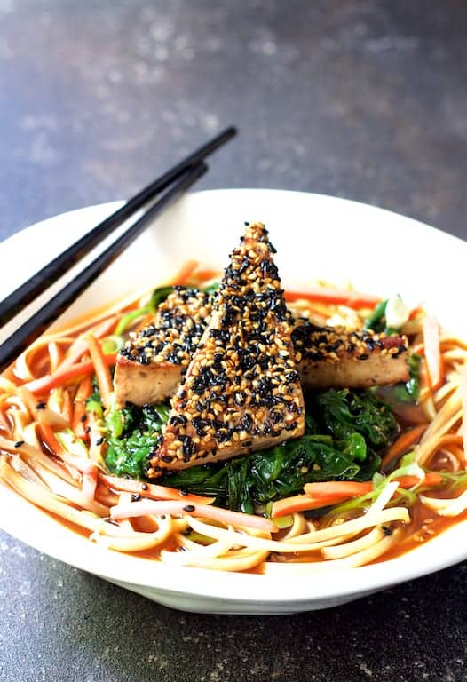 Photo of Sesame Tofu with Spinach and Rice Noodles in Ginger Broth in white bowl with black chopsticks on gray background.