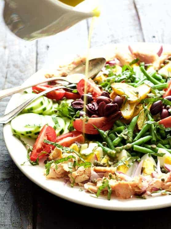 Salade Nicoise on white plate with fork and dressinf being drizzled over.