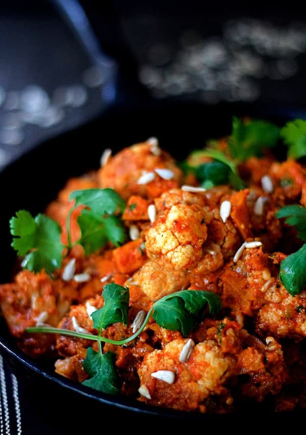 Photo of Cauliflower and Sweet Potatoes in Roasted Red Pepper Mole in cast iron skillet garnished with cilantro and sunflower seeds.