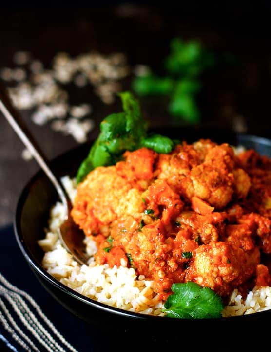 Cauliflower and Sweet Potatoes in Roasted Red Pepper Mole in black bowl with fork over brown rice.