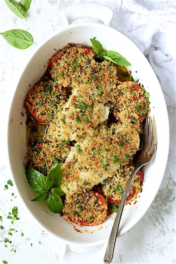 Photo of Pesto and Goat Cheese-Stuffed Chicken with Roma Tomatoes in white baking dish garnished with fresh basil.