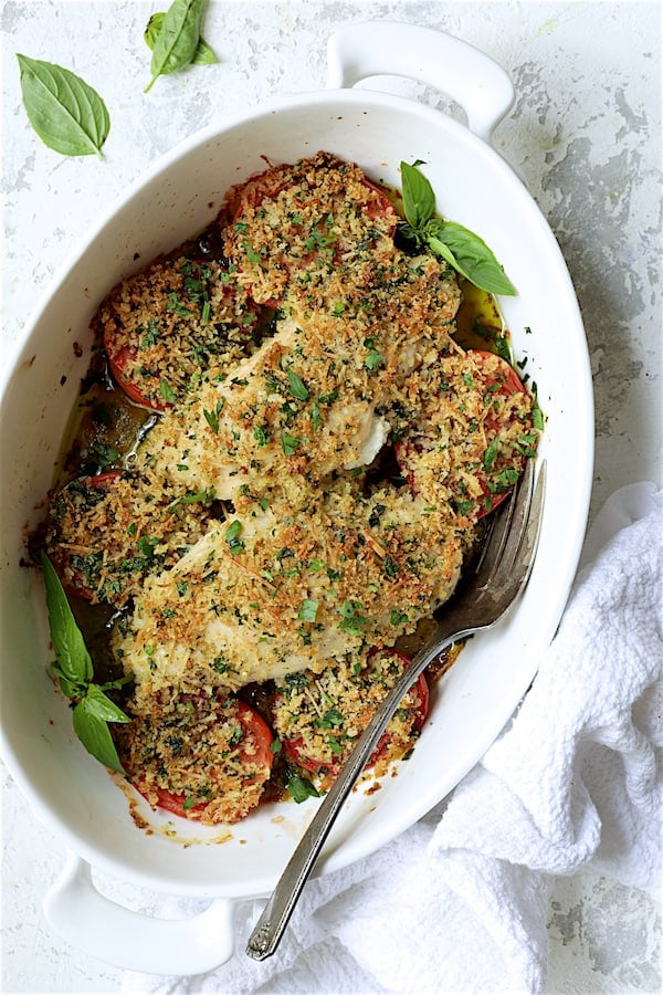 Photo of Pesto and Goat Cheese-Stuffed Chicken with Roma Tomatoes in white baking dish with serving fork.