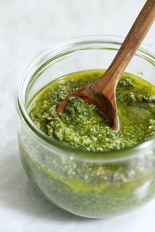 Photo of finished basil pesto in glass jar being stirred with wooden spoon.