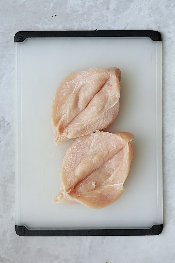 Photo of two butterflied chicken breasts on white cutting board.