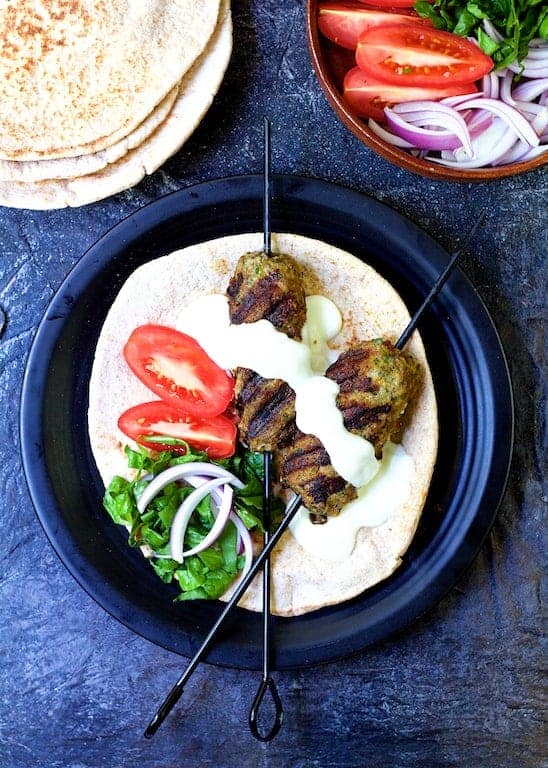 Grilled Turkish Ground Lamb Kebabs over pita bread on black plate.