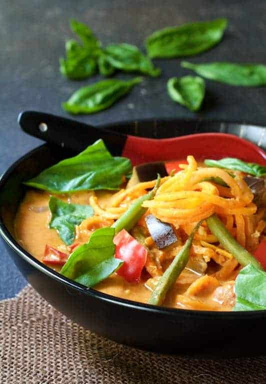 Vegetables in Thai Red Curry with Sweet Potato Noodles in black bowl with Asian-style spoon.