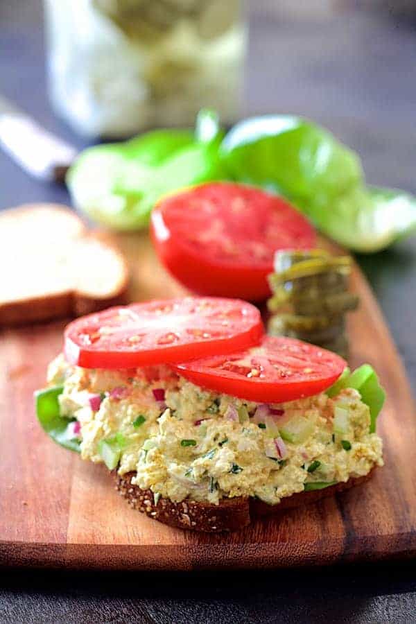 Photo of Curried Tofu Salad on whole-grain bread on wood cutting board with fresh lettuce and tomato.