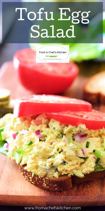 Pinterest graphic for Tofu Egg Salad showing it on bread on a wooden cutting board with tomatoes on top.