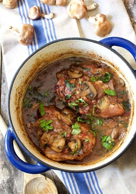Chicken Pinot Noir with Wild Mushrooms and Fresh Basil in blue Dutch oven on blue striped towel.