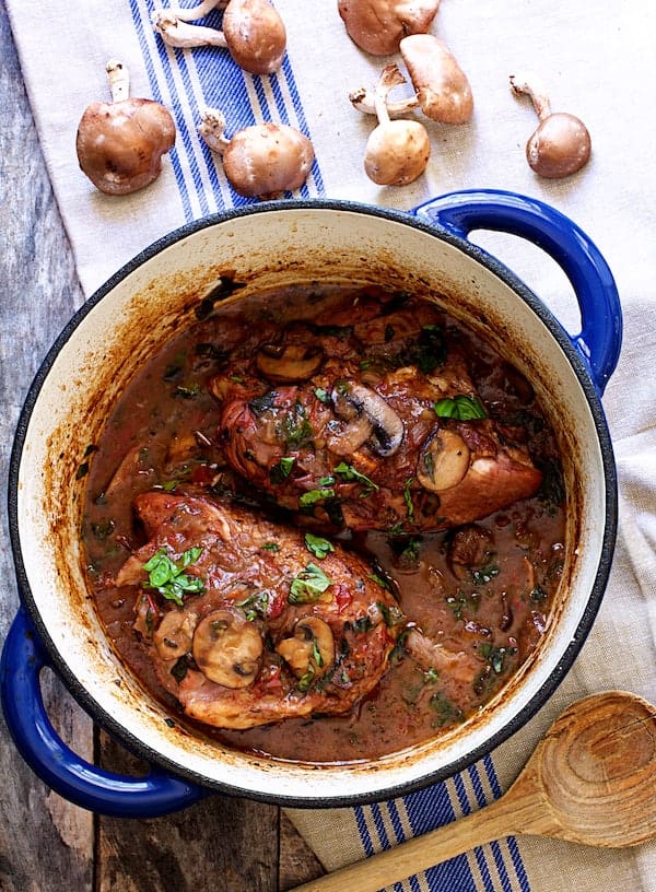Photo of Chicken Pinot Noir with Wild Mushrooms and Fresh Basil in blue Dutch oven on blue-striped towel.