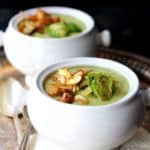 Two bowls of Cream of Brussels Sprouts Soup on decorative napkin with soup spoons on silver tray.