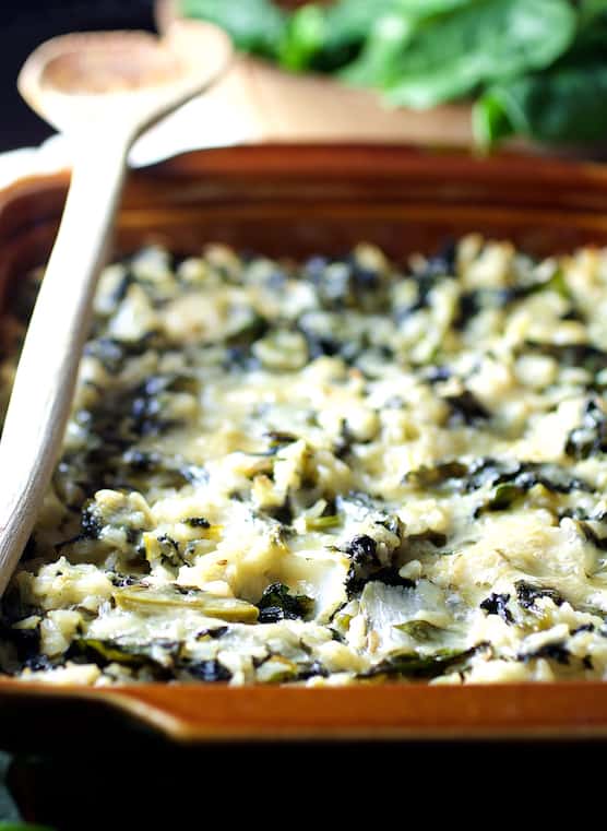 Photo of Cheesy Brown Rice and Greens Casserole in brown clay baking dish.