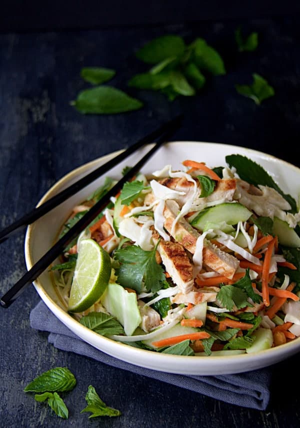 Photo of Vietnamese Chicken Salad with Spicy Lime Ginger Dressing in white bowl with black chopsticks on dark blue background.