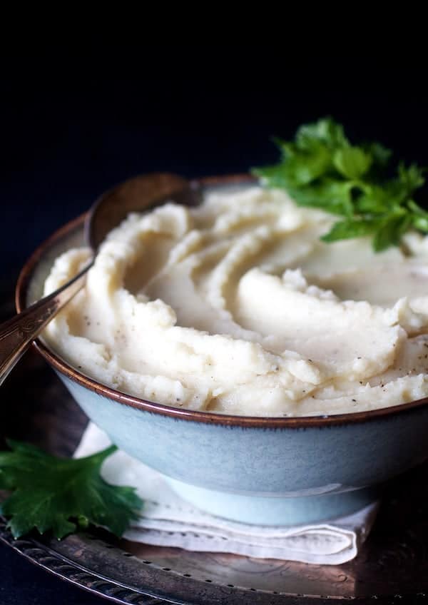 Photo of Celery Root Puree in gray bowl with serving spoon garnished with celery leaves.