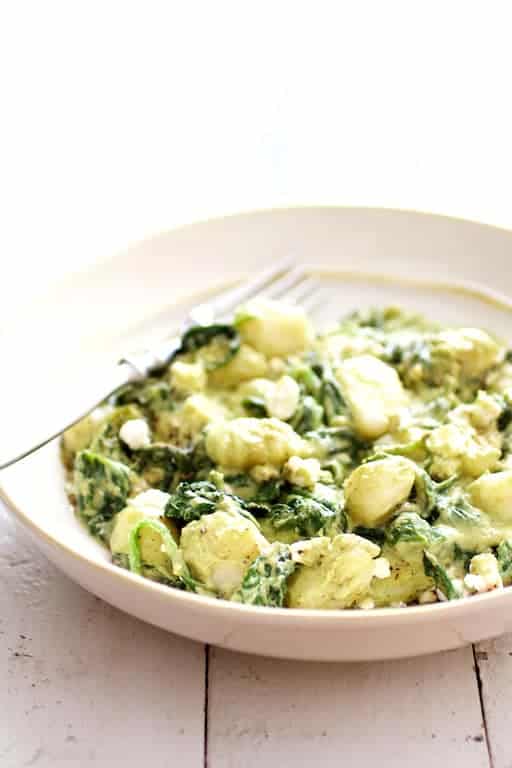 Photo of Gnocchi with Avocado Goat Cheese Sauce and Spinach in white bowl on white wood background.