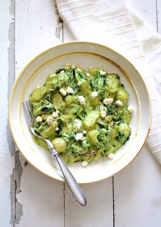 Photo of Gnocchi with Avocado Goat Cheese Sauce and Spinach on white distressed background with white napkin in white bowl.