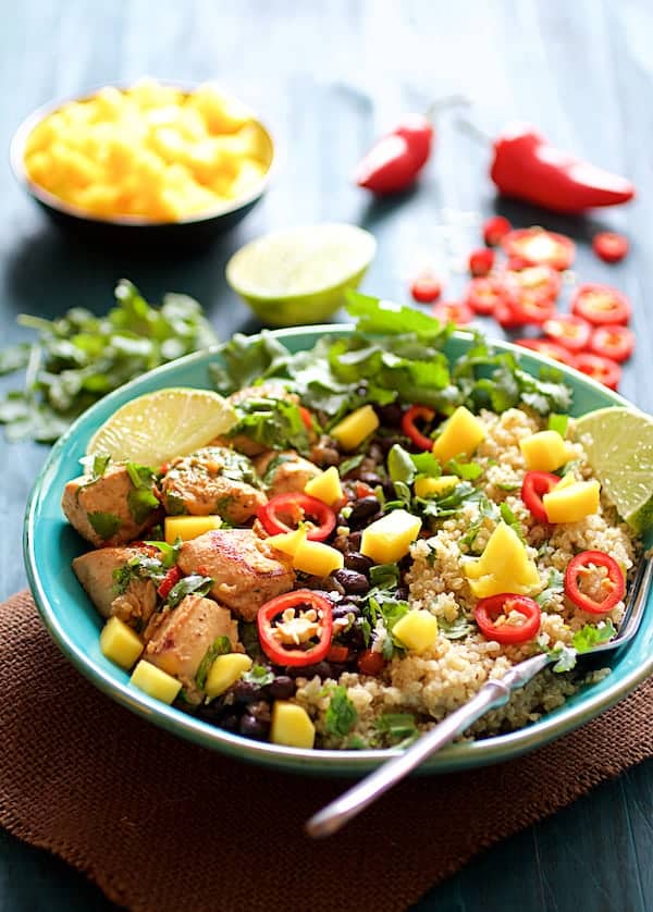 Photo of Cuban Chicken and Black Bean Quinoa Bowls on blue background garnished with mango, lime wedges, cilantro and Fresno chile.
