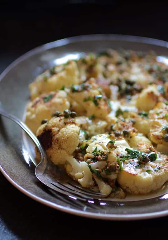 Photo of Roasted Cauliflower Steaks with Mustard Caper Brown Butter on gray-rimmed platter with serving fork.
