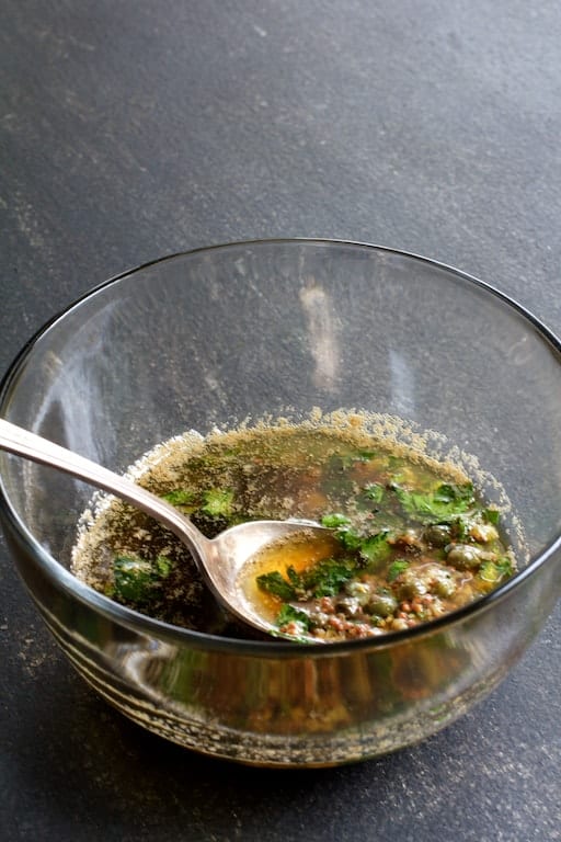 Photo of finished mustard caper brown butter in glass bowl on gray background.
