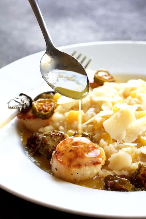 Seared Scallops with Jalapeño Browned Butter and Mango Buttermilk Risotto on white plate with spoon drizzling some of the butter over.