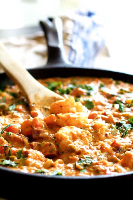 Photo of Smothered Shrimp and Andouille Sausage with Creamy Parmesan Peppercorn Grits being stirred with wooden spoon in cast iron skillet.