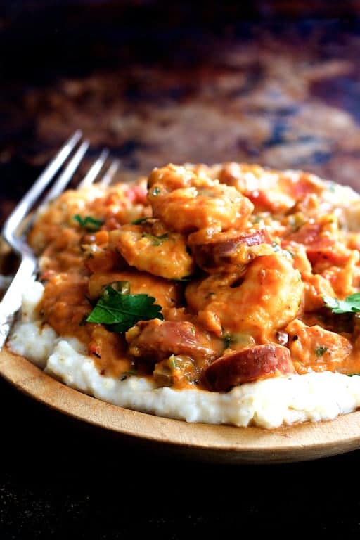 Photo of one serving of Smothered Shrimp and Andouille Sausage with Creamy Parmesan Peppercorn Grits in wooden bowl with fork.