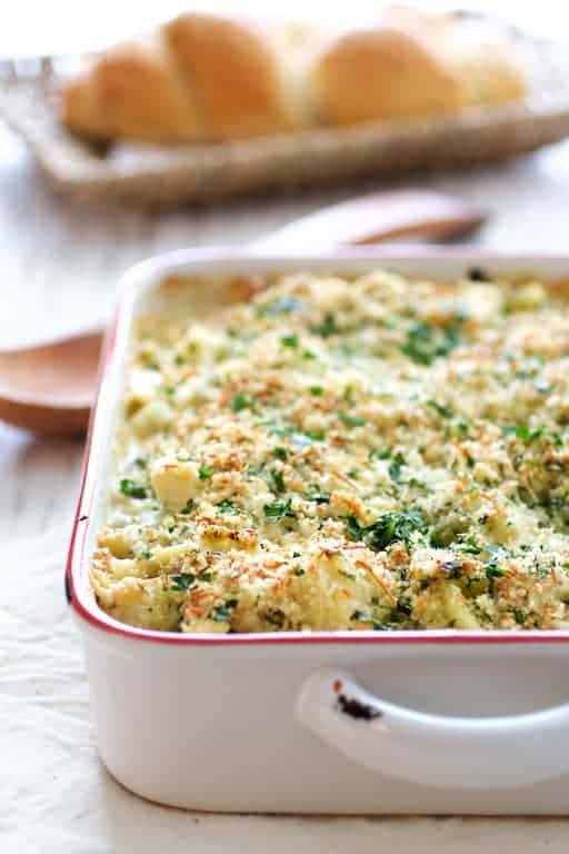 Photo of Baked Orecchiette with Cauliflower, Bacon and Taleggio in white baking dish on white surface with bread in the background.