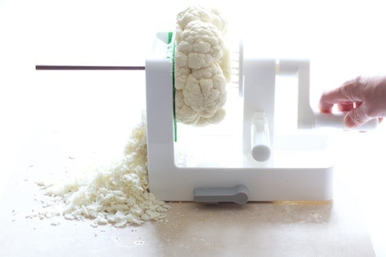 Photo of cauliflower being shredded in a vegetable spiralizer.