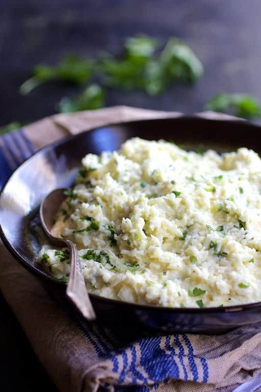 Photo of Cauliflower Grits with Gouda Cheese in black bowl with serving spoon on blue striped towel.
